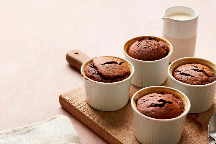 Four white ramekins filled with chocolate souffles, set on a wooden board