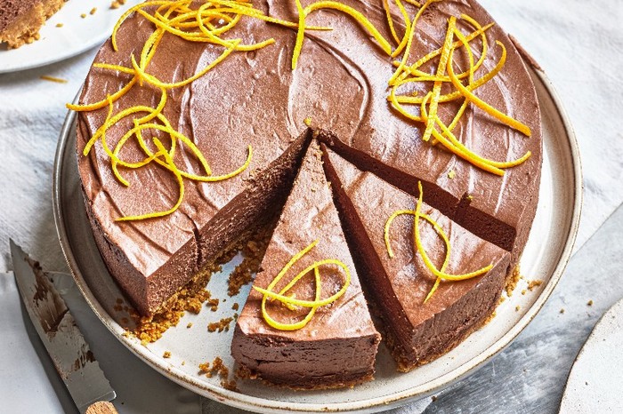 A chocolate cheesecake on a white plate with strips of orange zest on top