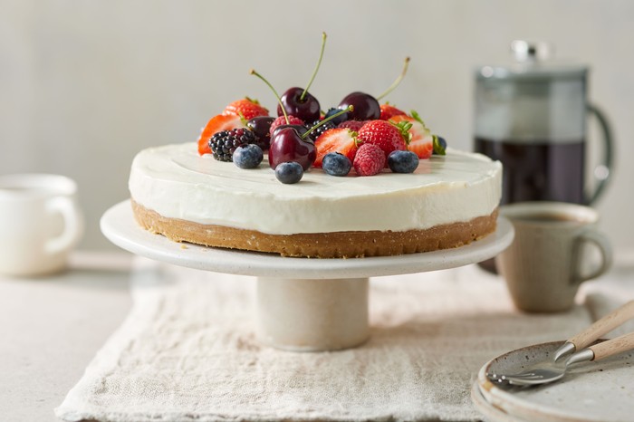 A classic vanilla cheesecake topped with summer berries, presented on a cake stand