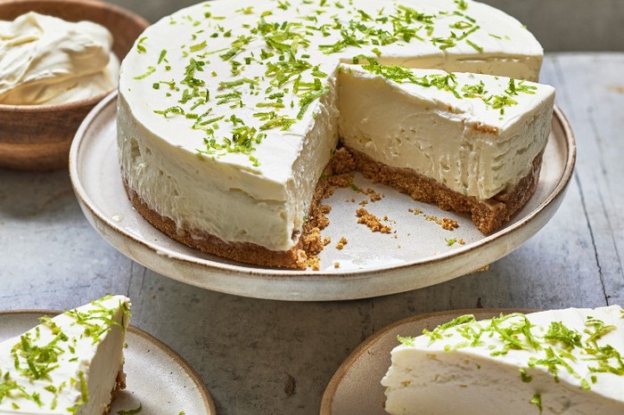 A cheesecake topped with lime zest on a cake stand with a slice taken out