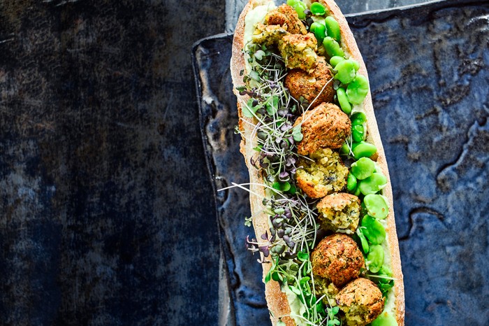 Falafel with Avocado Hummus Recipe and Broad Beans served in a crispy white baguette on a dark blue tray and table
