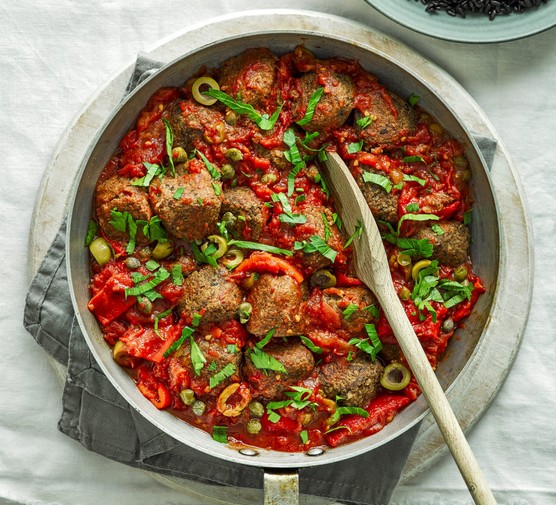 Veggie meatballs in a large pot with a wooden spoon placed inside it