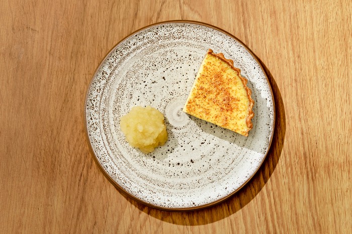a white plate on a wooden background, with a slice of custard tart and dollop of apple compote
