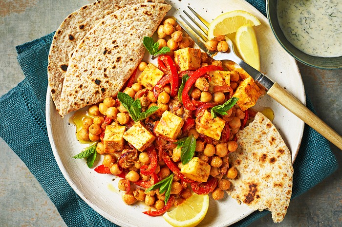 A white plate topped with a chickpea and paneer curry with two chapatis on the side