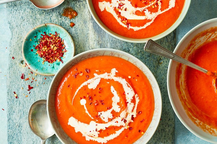 Several bowls of red pepper soup, with a swirl of creme fraiche