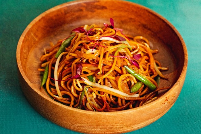 A wooden bowl filled with noodles and veg on a green background